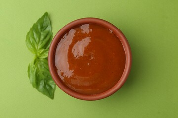 Tasty curry sauce and basil leaves on green background, top view