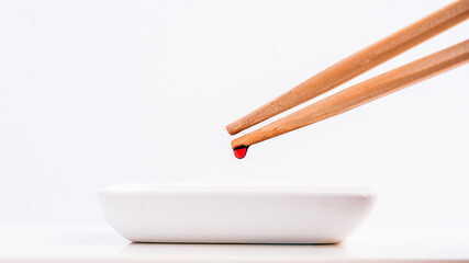 Close-Up of Chopsticks with Sauce Drop Over White Plate