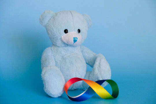 Autism acceptance month, Autism awareness day concept. Toy teddy bear with rainbow colors ribbons in shape of infinity on blue background. Infinity is symbol of autism disorder, ADHD, neurodiversity