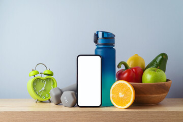 Fitness background with bottle of water, dumbbells, healthy food and smart mobile phone on wooden table. Mock up template for fitness app