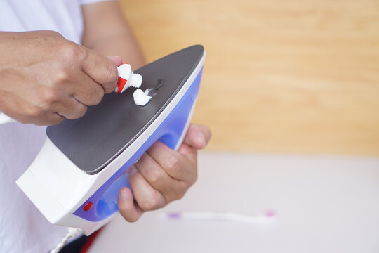 Close up hand squeeze toothpaste to clean stain on iron appliance surface. Concept, household tool treatment maintenance. Repair, electric equipment. Trick for solving problems burning stain.     