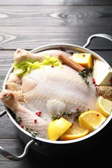 Whole raw turkey, citrus fruits and spices in pot on black wooden table, closeup