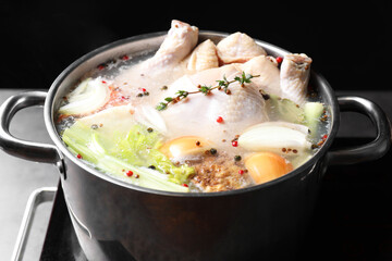Whole fresh turkey, cut onion, celery and spices boiling in pot on stove against black background, closeup