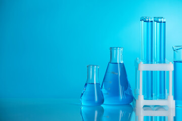 Laboratory glassware with liquid on mirror surface against blue background. Space for text