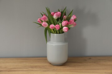 Bouquet of beautiful tulips in vase on wooden table against light grey background