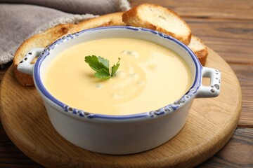 Tasty cheese dipping sauce in bowl and croutons on wooden table, closeup