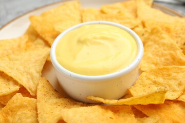 Tasty cheese dipping sauce in bowl and nacho chips on table, closeup