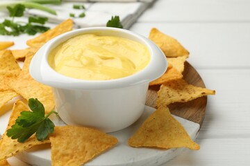 Tasty dipping cheese sauce in bowl and nacho chips on white wooden table, closeup