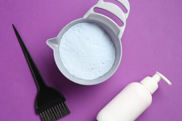 Bowl with hair bleaching powder, bottle of developer and brush on purple background, flat lay