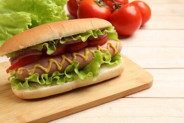 Tasty hot dog with tomatoes, onion, lettuce and mustard on wooden table, closeup