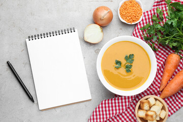 Blank recipe book, lentil cream soup and ingredients on light grey table, flat lay