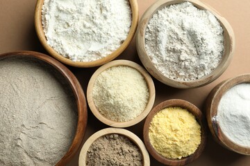 Different types of flour on light brown table, flat lay