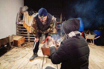 Two people tending a fire pit in a cluttered backyard at night with smoke.
