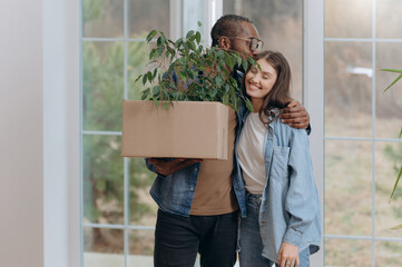 Couple Embracing While Holding a Potted Plant in a Bright Home