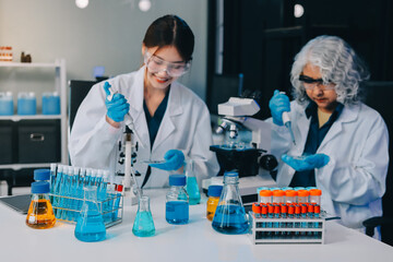 Fototapeta premium Asian people scientist in lab coat and protective gloves working with test tubes with green and red liquids, with microscope and other test tubes in the background in laboratory.