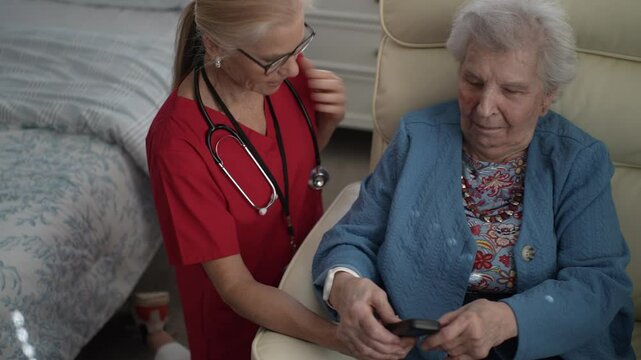 A caregiver interacts with an elderly woman, assisting her with a device in a healthcare facility. The setting promotes memory care and engagement.