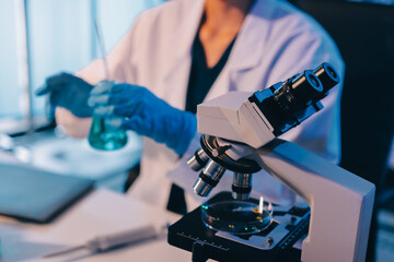 Two Asian women in a lab work on food research, using a microscope, petri dish, and test tubes filled with chemical solutions. They study vegetables, pork, and plants for GMO traits and nutrition.
