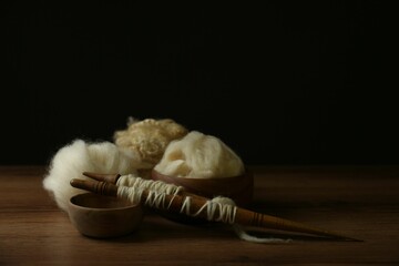 Spindles and soft white wool on wooden table against black background, space for text