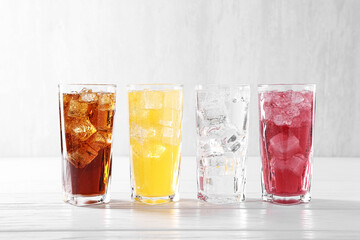 Soda water of different flavors with ice cubes in glasses on white wooden table