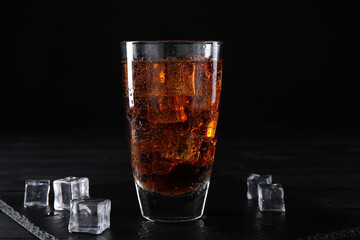 Sweet soda water in glass with ice cubes on black wooden table