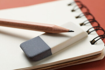 Eraser, pencils and notebook on brown background, closeup