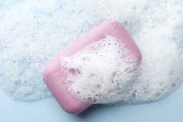 Soap bar with foam on light blue background, top view
