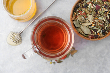 Delicious herbal tea with honey and dry leaves on grey table, flat lay