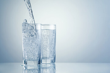 Pouring refreshing soda water into glasses on light grey background, closeup. Space for text