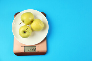 Electronic kitchen scale with plate of apples on light blue background, top view. Space for text