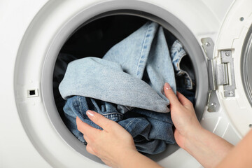 Woman putting jeans into washing machine, closeup