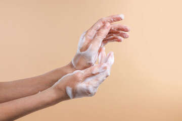 Woman washing hands with foaming soap on beige background, closeup. Hygiene