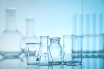Laboratory glassware on mirror surface against light blue background