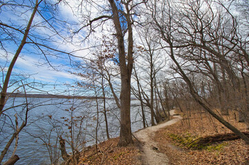 Early Spring landscape of a hiking trail beside the Illinois River beneath a partly cloudy blue sky at Starved Rock State Park near Oglesby, Illinois.