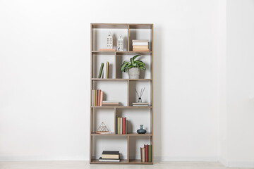 Wooden shelving unit with different home decor and houseplant near white wall indoors © New Africa