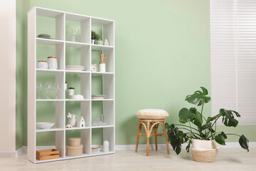 Fototapeta premium Shelving unit with dishware near olive wall indoors. Space for text