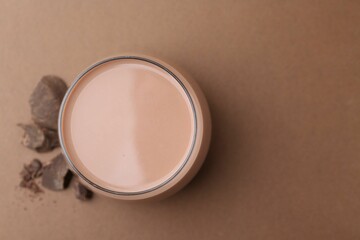 Tasty chocolate milk in glass and pieces of chocolate on brown background, flat lay. Space for text