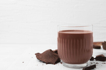 Tasty chocolate milk in glass and pieces of chocolate on white tiled table, closeup. Space for text