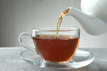 Pouring freshly brewed tea from teapot into cup at grey table, closeup