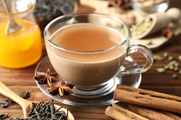 Aromatic Masala tea in cup, spices, dry leaves and honey on wooden table, closeup