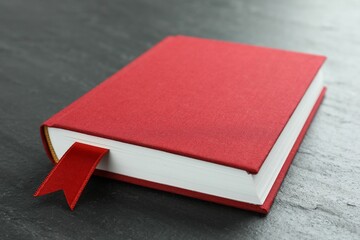 Book with red ribbon bookmark on dark textured table, closeup