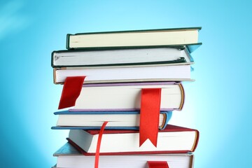 Books with red ribbon bookmarks on light blue background, closeup