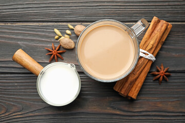 Aromatic Masala tea in glass cup, milk and spices on wooden table, flat lay
