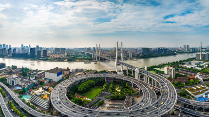 Panoramic of Shanghai featuring a complex highway interchange system, Huangpu River, cityscape under a blue sky with clouds showcasing urban transport as a background