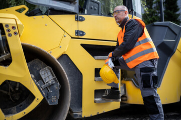 Construction worker preparing to operate a road roller on a work site in daylight wearing safety gear