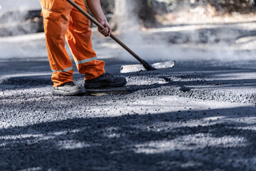 Worker applies asphalt to repair road in late morning sunlight in urban area