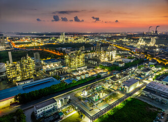 Fototapeta premium Aerial view of illuminated industrial zone with refineries, factories and colorful sky at dusk