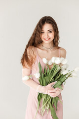 young european lady in pink dress hugging bouquet of white tulips on isolated white background 
