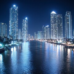 Fototapeta premium Night view of a city skyline with illuminated skyscrapers reflected in a calm waterway. Cool blue tones dominate the scene, creating a serene atmosphere.