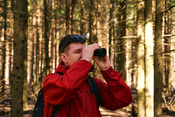 A man looks through monocular binoculars in the woods in nature. Search for new opportunities