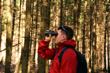 A man looks through monocular binoculars in the woods in nature. Search for new opportunities